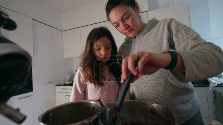Madre preparando la comida junto a su hija mientras su hijo deambula por la cocina, auténtica escena de estilo de vida familiar padre cocina sosteniendo espátula en la mano mezclando ingredientes