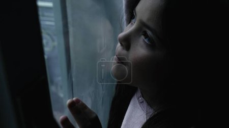Photo for Lonely child feeling sad and depressed in moody winter scene by glass window. One thoughtful little girl stuck at home - Royalty Free Image