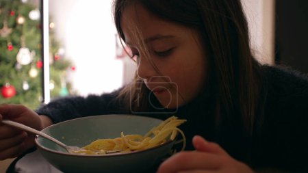 Foto de Una niña pequeña comiendo pasta en casa para la hora de comer. La cara de niño come fideos espagueti - Imagen libre de derechos