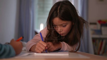 Téléchargez les photos : Petite fille dessin avec stylo à colorier dans la table de chambre à coucher, temps libre de développement de l'art de l'enfance. Enfant féminin engagé dans un effort créatif - en image libre de droit