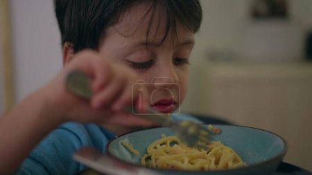 Photo for One little boy eating spaghetti noodles for dinner time by himself. Child using fork to eat pasta food - Royalty Free Image