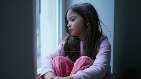 Photo for Child Feeling Lonely at Home, Struggling with Difficulties in Childhood. Little girl gazing at view from apartment window, lost in thought feeling sad and depressed - Royalty Free Image