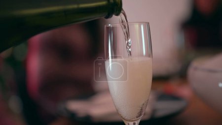 Téléchargez les photos : Verser du champagne dans un verre célébrant les fêtes, les gens déconcentrés en arrière-plan - en image libre de droit
