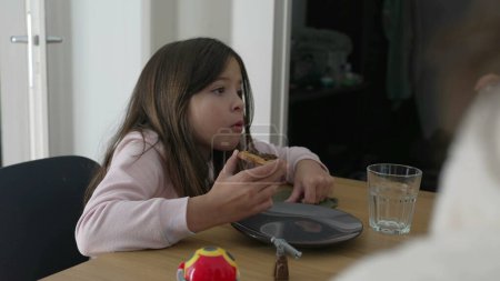 Ein kleines Mädchen beim Essen interagiert außerhalb der Kamera mit der Familie. Kind nascht Efiha