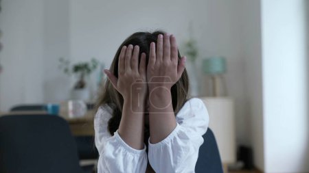 Photo for Child regretting past mistakes by covering face in shame and hitting her own head and forehead with hand. Little girl in disapproval, lamenting errors - Royalty Free Image