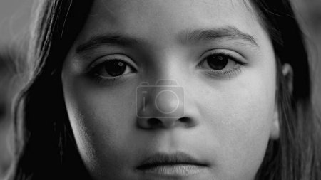 Serious little girl close-up face staring at camera in black and white, monochrome. Macro portrait with solemn sad pensive expression