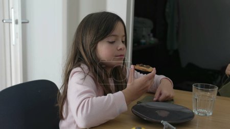 Una niña comiendo durante la hora de la comida interactuando con la familia fuera de cámara. Snacking infantil esfiha