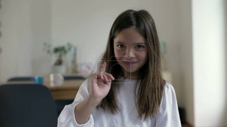 Foto de Una niña pequeña rechazando la oferta agitando el dedo al espectador mientras sonríe. Niño defendiendo acusación saludando con la mano diciendo NO - Imagen libre de derechos