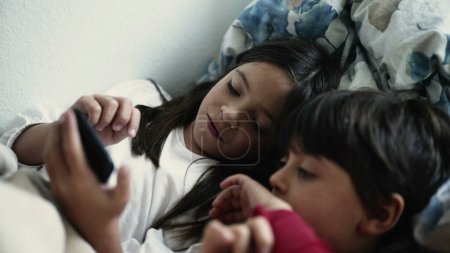 Photo for Brother and Sister Engrossed in Smartphone Screen While Lying in Bed, Siblings Bonding Over Digital Device - Royalty Free Image