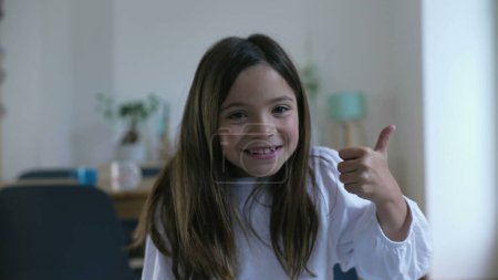Téléchargez les photos : Une petite fille excitée donnant pouces jusqu'à la caméra souriant, enfant de 8 ans montrant un signe d'approbation - en image libre de droit