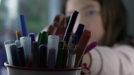 Photo for Coloring pens inside bucket in foreground with little girl in blurred background grabbing a pen during creative drawing session - Royalty Free Image