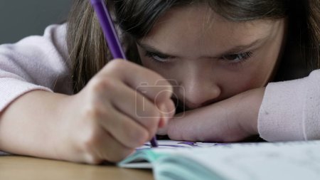 Téléchargez les photos : Focalisé enfant bouleversé dessin sur papier sentiment de colère profonde tout en tenant un stylo à coloration tout en pensant à des problèmes mentaux dans l'enfance - en image libre de droit
