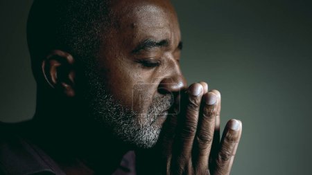Photo for Earnest African American Elder Seeking Divine Guidance in Prayer, Eyes Shut and Hands Together, Senior Man in Deep Contemplation Asking for Help and Support - Royalty Free Image