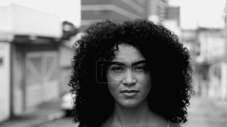 Téléchargez les photos : Intense Gaze of African American Young Woman in Street, Black and White Close-Up Face in Urban Environment. Une fille adulte brésilienne dans les années 20 avec des cheveux bouclés avec une expression de confiance sévère - en image libre de droit