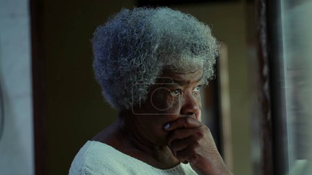 Téléchargez les photos : Une contemplative femme noire des années 80 âgée debout à la maison avec la main sur le menton réfléchissant profondément sur les problèmes, expression coûteuse de afro-américaine dame aux cheveux gris - en image libre de droit