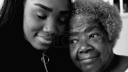 Téléchargez les photos : Liaison intergénérationnelle - Petite-fille afro-américaine et grand-mère aînée dans un moment tendre affectueux, jeune fille qui prend soin de sa grand-mère âgée dans la vieillesse, noir et blanc - en image libre de droit