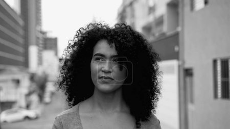 Photo for Empowered Young Brazilian Woman with Curly Hair Striding in City Street in intense black and white. One thoughtful South American latin person walking forward - Royalty Free Image
