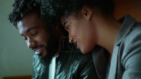 Téléchargez les photos : Couple afro-américain partage écran de téléphone portable, jeune femme appuyé sur l'épaule de l'homme en regardant le contenu en ligne souriant, scène franche de personnes consommant des médias sociaux en ligne - en image libre de droit