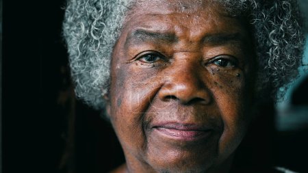 Eine ernstzunehmende schwarze ältere Dame blickt in die Kamera und präsentiert Erfahrung und Weisheit. Afroamerikanische Seniorin der 80er Jahre mit Falten und grauen Haaren Porträt Gesicht Nahaufnahme