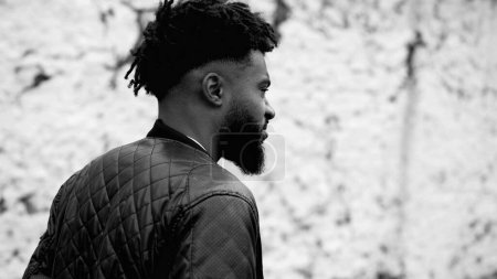 Photo for One thoughtful young black walks forward in urban setting contemplating life while strolling outdoors in monochromatic, black and white. Tracking shot of a pensive 20s person, moody introspection - Royalty Free Image