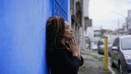 Foto de Una latina negra hispana de ascendencia africana en contemplación mental durante tiempos difíciles en busca de ayuda divina y apoyo mirando hacia el cielo en oración de pie en la calle afuera - Imagen libre de derechos