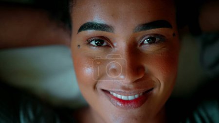 Photo for One young black latin woman opening eyes and looking directly at camera and smiling exuding confidence and awakening. 20s African American person - Royalty Free Image