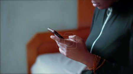 Foto de Una joven mujer negra usando el dispositivo de teléfono celular en el dormitorio, las manos de cerca y la cara de perfil comprometidos con la tecnología moderna, mirando a la pantalla - Imagen libre de derechos