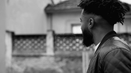 Ein aggressiver afroamerikanischer junger Mann schlendert durch die urbane Stadtstraße und filmt eine nachdenkliche, nachdenkliche schwarze Person in monochromen Schwarz-Weiß. Introspektive Spaziergangsemotion