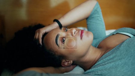 Téléchargez les photos : Une femme latina noire sud-américaine fatiguée réfléchie couchée au lit joue avec elle tout en étant perdue dans la contemplation tout en réfléchissant à la décision et en se reposant dans une solitude tranquille - en image libre de droit