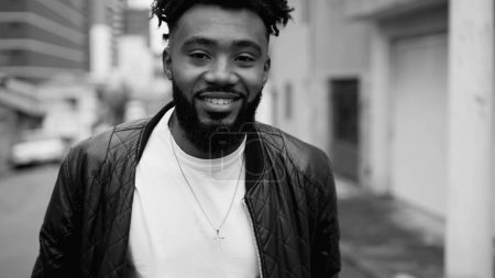 Téléchargez les photos : Un jeune homme noir heureux marchant vers l'avant en milieu urbain, noir et blanc monochromatique dans le suivi de tir - en image libre de droit