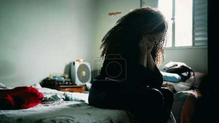 Téléchargez les photos : Une femme latina noire mature désespérée assise au chevet du lit couvrant le visage regrettant les erreurs passées à l'intérieur de la chambre à coucher se sentant submergée par des problèmes. Afro-américain face à l'anxiété - en image libre de droit
