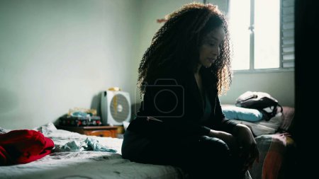 Photo for One desperate mature black latina woman seated by bedside covering face regretting past mistakes inside bedroom feeling overwhelmed by problems. African American person facing anxiety - Royalty Free Image