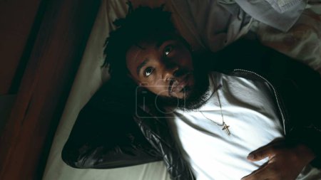 Foto de Un joven negro reflexivo descansando y soñando despierto mientras está acostado en la cama expresando la mirada contemplativa reflejando la vida. Afrodescendiente 20s persona toma un descanso - Imagen libre de derechos
