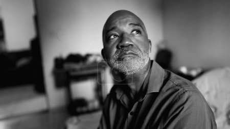 Homme âgé afro-américain déprimé réfléchi avec de tristes luttes émotionnelles dans la solitude dans la chambre lunatique en noir et blanc dramatique, portrait monochrome