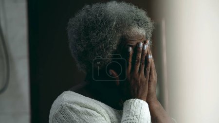 Bedauernswerte afroamerikanische ältere Frau in den Achtzigern, die Gesicht mit Händen bedeckt, die Angst und Sorge über schwierige Umstände im Alter empfinden, wenn sie zu Hause steht