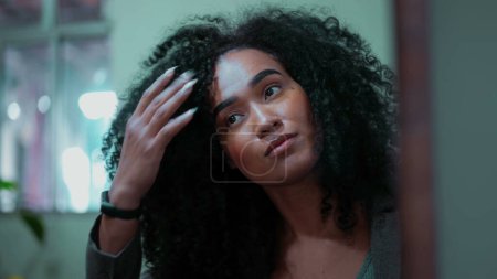 Foto de Joven mujer afroamericana de 20 años preparándose para salir, juega con el pelo rizado y ajustar el peinado antes de salir, cara clsoe-up - Imagen libre de derechos