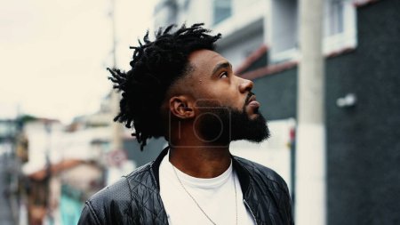 Photo for Young African American man gazing up at sky close-up face. One young black 20s person looking skyward in urban street environment during drizzle rain - Royalty Free Image