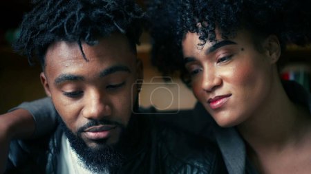 Photo for Young man and woman staring at cellphone device screen off-camera. South American 20s people of African descent watching entertainment media online, sharing screen, girl with arm around partner - Royalty Free Image
