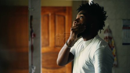 Photo for One worried young black man standing by window at home with pensive thoughtful expression. Preoccupied African American person contemplating solution to problems - Royalty Free Image