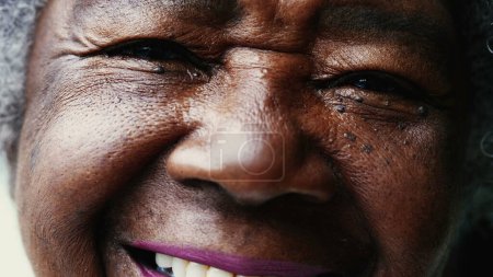 Téléchargez les photos : Macro gros plan d'une heureuse femme noire âgée souriant à la caméra avec le visage ridé montrant la sagesse et la vieillesse. Portrait d'une Afro-Américaine dans les années 80 - en image libre de droit