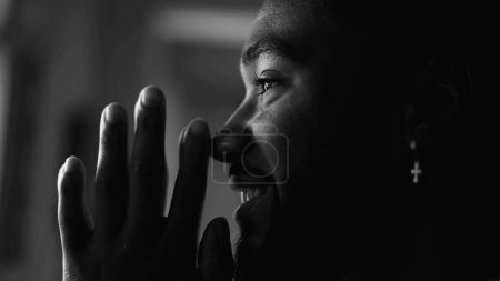 Photo for One happy young black man PRAYING in feeling HOPEFUL. Faithful African American person profile close-up face smiling in black and white, monochromatic - Royalty Free Image
