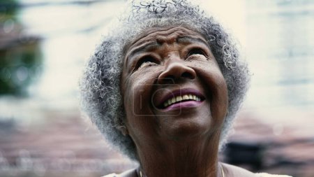 Foto de Esperanzada mujer afroamericana mayor mirando al cielo durante la lluvia con FE y ESPERANZA. Una dama negra de pelo gris girando la cabeza hacia arriba - Imagen libre de derechos