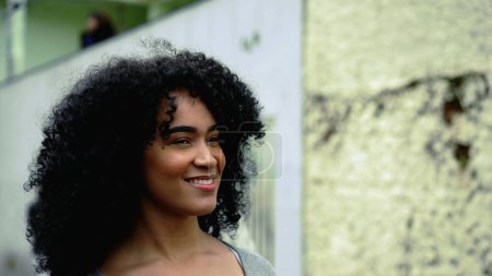 Une jeune femme afro-américaine autonomisée marche en avant dans la rue, suivi plan rapproché visage de la fille adulte aux cheveux bouclés confiante dans les années 20 exsudant joie et bonheur