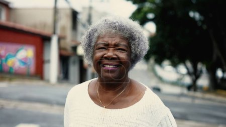 Téléchargez les photos : Une femme âgée noire mature marchant dans la rue de la ville à l'extérieur. Femme âgée afro-américaine dans les années 80 se promener dans l'environnement urbain en regardant la caméra - en image libre de droit