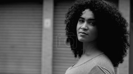 Empowered African American Woman in Urban Setting, Tracking Close-Up of Confident Young Female Face in bold black and white, monochromatic. One black person standing in street staring at camera