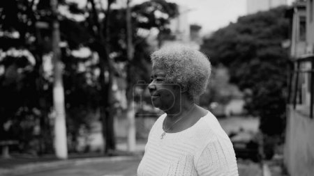Photo for One older black woman in 80s walking in urban setting, tracking shot body of African American elderly lady with gray hair strolling in street, black and white - Royalty Free Image