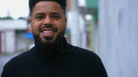 Photo for One happy young black Brazilian man walking in city street forward toward camera smiling. 20s South American person in urban environment portrait - Royalty Free Image