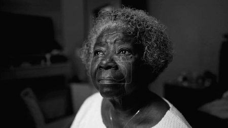 Téléchargez les photos : Une dame noire âgée réfléchie assise au chevet du lit à la maison seule regardant la fenêtre de la chambre. Méditatif cheveux gris sud-américain femme plus âgée dans le regard paisible - en image libre de droit