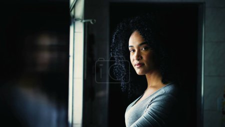 Photo for Happy Portrait of a young black Brazilian woman turning head to camera smiling standing by window at home. Curly hair South American adult girl smiling - Royalty Free Image