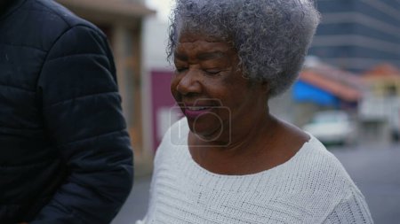 Señora mayor afroamericana paseando por la calle con la ayuda de su hijo adulto de mediana edad cuidador, caminando hacia adelante en el seguimiento de tiro wiht movimiento en el entorno urbano
